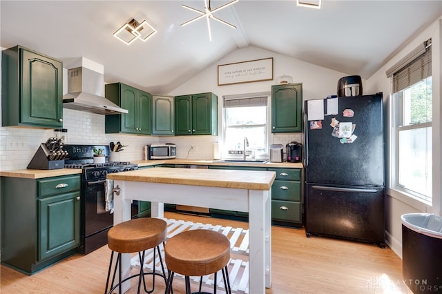 kitchen with sink, wall chimney exhaust hood, green cabinets, lofted ceiling, and black appliances