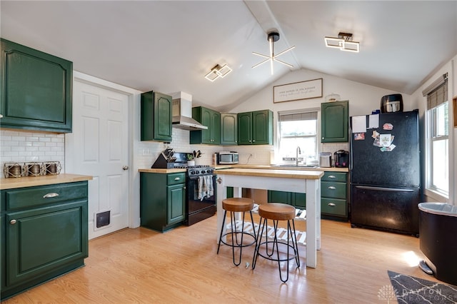 kitchen featuring black appliances, green cabinets, vaulted ceiling, wall chimney exhaust hood, and light hardwood / wood-style floors