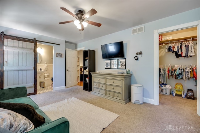 carpeted bedroom featuring a barn door, a closet, ceiling fan, and connected bathroom