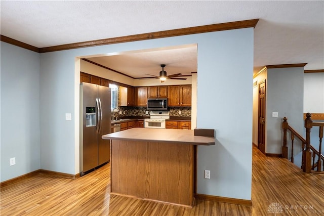 kitchen with kitchen peninsula, light wood-type flooring, tasteful backsplash, ornamental molding, and stainless steel appliances