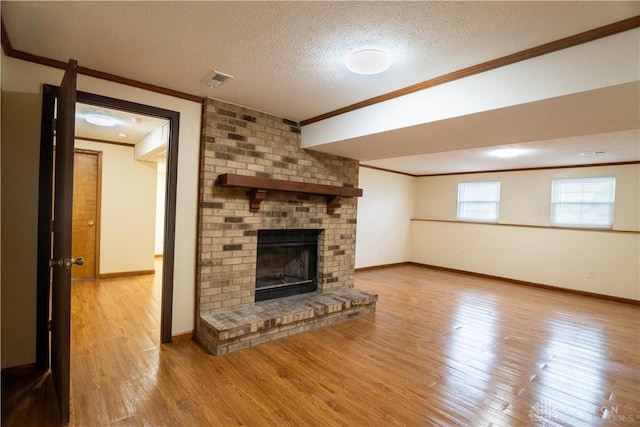 unfurnished living room with a fireplace, light wood-type flooring, a textured ceiling, and ornamental molding