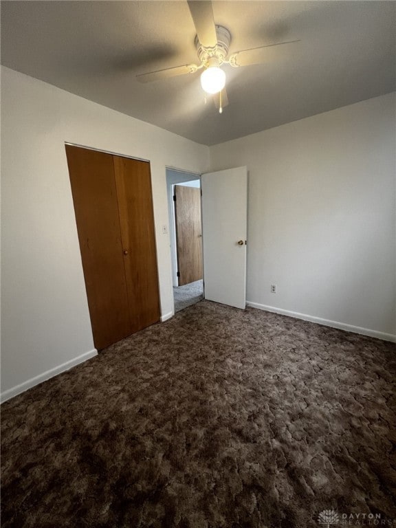 unfurnished bedroom featuring dark colored carpet, a closet, and ceiling fan