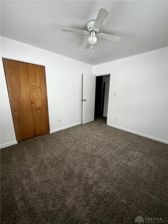 unfurnished bedroom with ceiling fan, dark carpet, and a closet