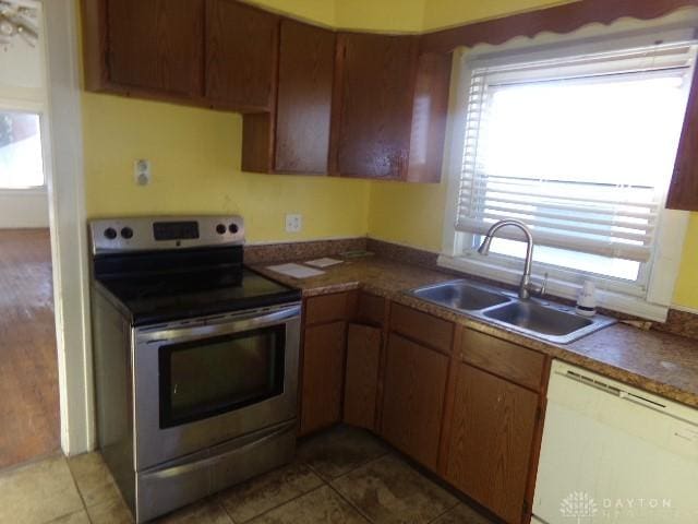 kitchen with dishwasher, dark tile patterned floors, stainless steel range with electric stovetop, and sink