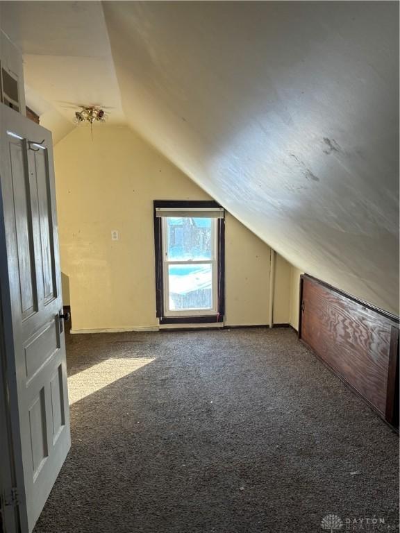 bonus room with dark carpet and vaulted ceiling