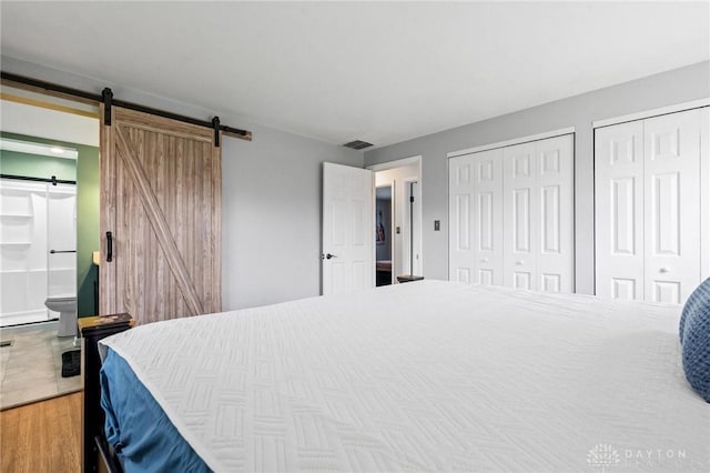 bedroom with ensuite bathroom, a barn door, wood-type flooring, and multiple closets