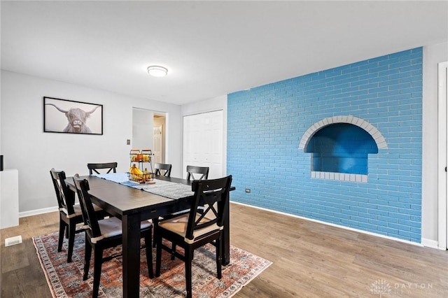 dining room featuring hardwood / wood-style flooring and brick wall