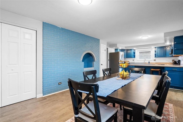 dining space with light hardwood / wood-style floors and brick wall