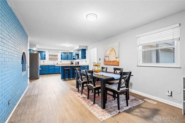 dining area featuring sink, brick wall, and light hardwood / wood-style flooring