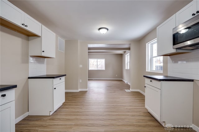 kitchen with light wood-type flooring, backsplash, white cabinetry, and a healthy amount of sunlight