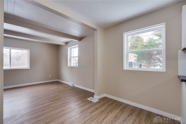 unfurnished room with beamed ceiling, plenty of natural light, and light hardwood / wood-style floors