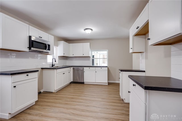 kitchen with white cabinets, appliances with stainless steel finishes, decorative backsplash, and light hardwood / wood-style flooring