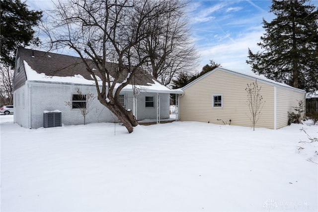 snow covered rear of property featuring central AC