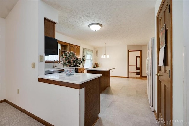 kitchen with kitchen peninsula, a textured ceiling, hanging light fixtures, an inviting chandelier, and sink