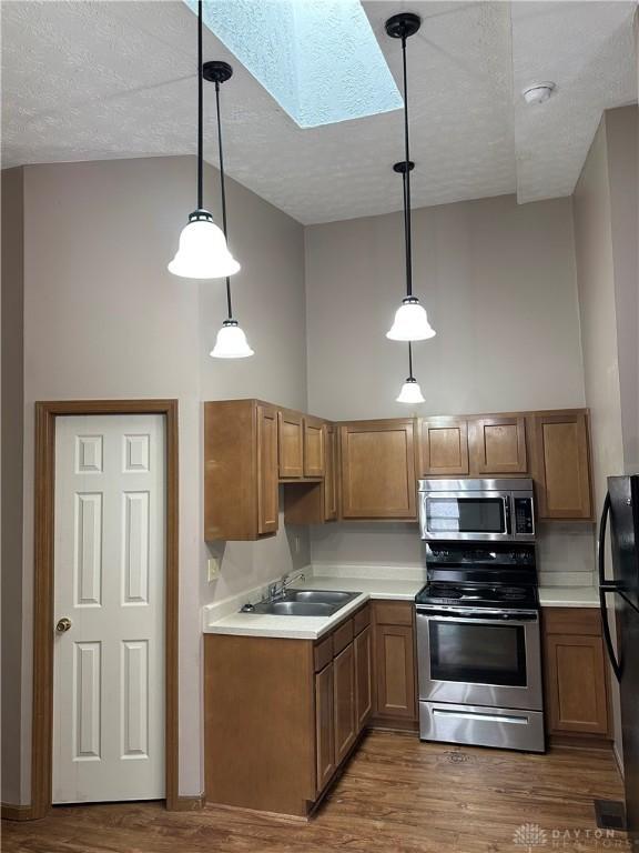 kitchen featuring appliances with stainless steel finishes, hanging light fixtures, a skylight, high vaulted ceiling, and dark hardwood / wood-style floors