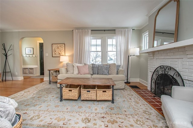 living room featuring ornamental molding, a brick fireplace, and wood-type flooring