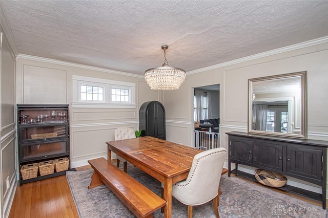 dining space with hardwood / wood-style flooring, ornamental molding, a textured ceiling, and an inviting chandelier