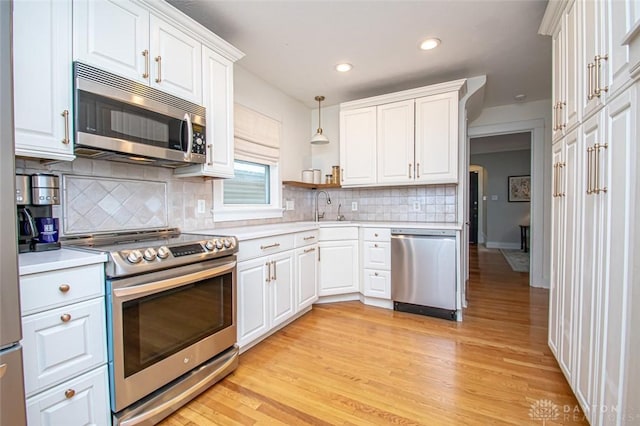 kitchen featuring decorative light fixtures, sink, white cabinets, stainless steel appliances, and light wood-type flooring