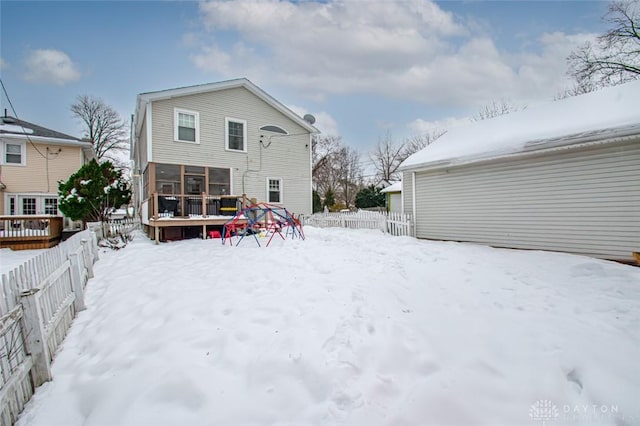 snow covered back of property featuring a wooden deck and a sunroom