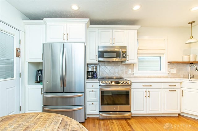 kitchen featuring sink, white cabinetry, hanging light fixtures, stainless steel appliances, and light wood-type flooring