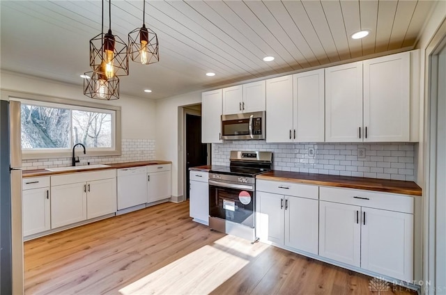 kitchen with hanging light fixtures, stainless steel appliances, wood counters, white cabinets, and sink