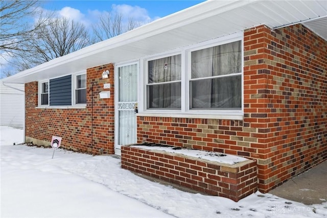 snow covered property entrance featuring brick siding