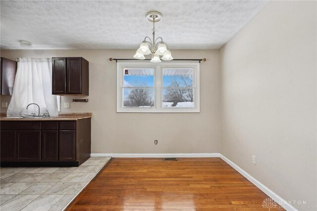 unfurnished dining area with an inviting chandelier, light wood-type flooring, and a textured ceiling