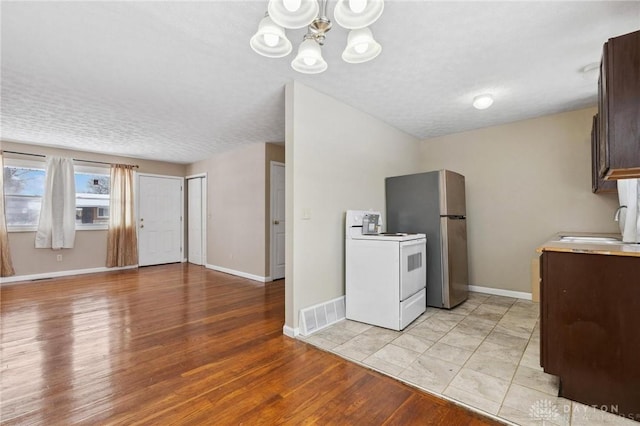 kitchen featuring white range with electric stovetop, visible vents, light wood-style flooring, freestanding refrigerator, and a sink