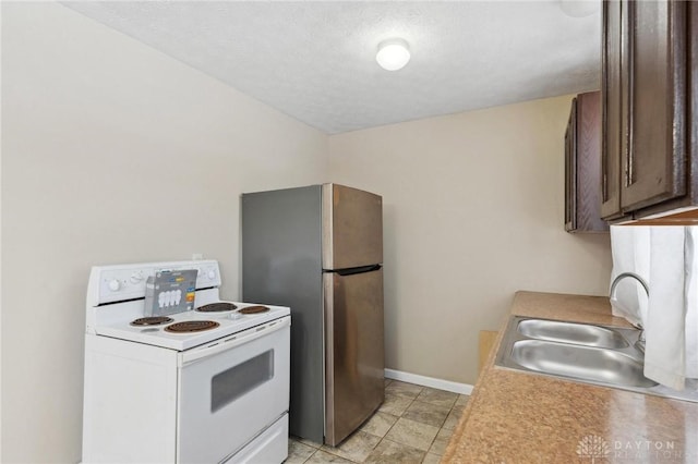 kitchen with baseboards, freestanding refrigerator, light countertops, white electric range, and a sink