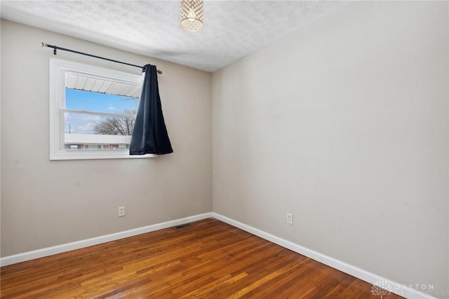 unfurnished room featuring a textured ceiling, wood finished floors, visible vents, and baseboards