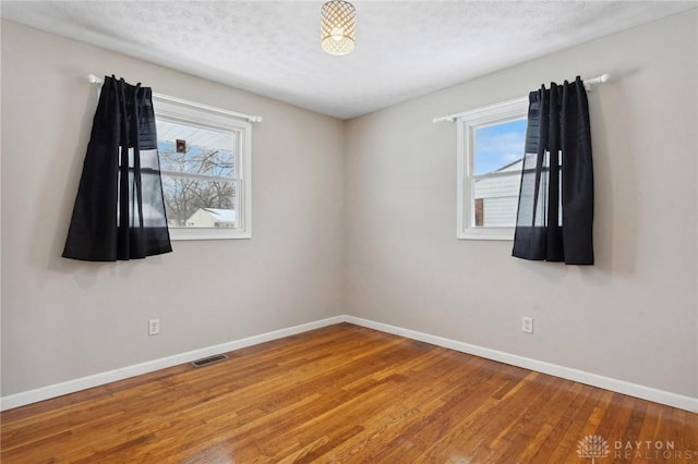 spare room with visible vents, a textured ceiling, baseboards, and wood finished floors