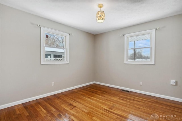 spare room featuring baseboards, wood finished floors, visible vents, and a healthy amount of sunlight