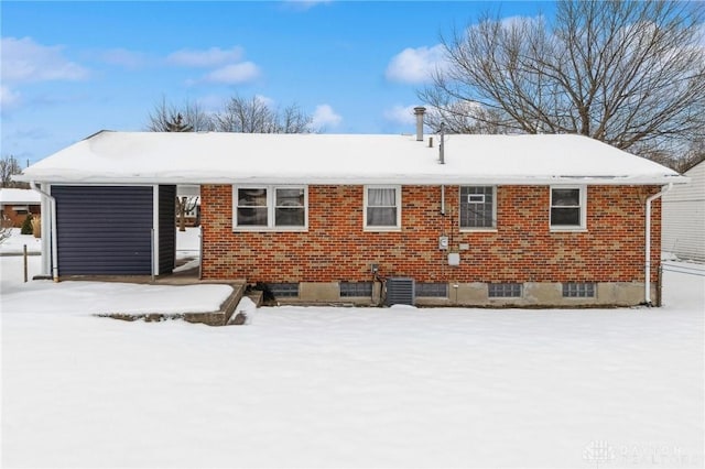 snow covered property with a garage, brick siding, and central AC unit