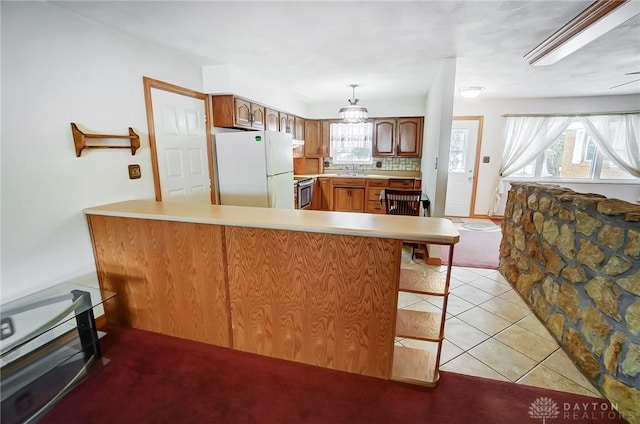 kitchen featuring white fridge, kitchen peninsula, decorative light fixtures, stove, and light tile patterned flooring