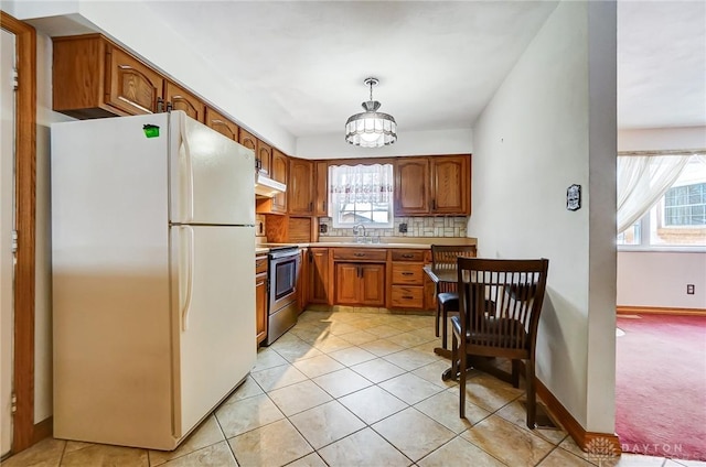 kitchen with white refrigerator, stainless steel electric range, a healthy amount of sunlight, and a notable chandelier