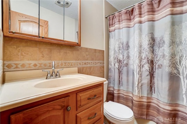 bathroom featuring toilet, walk in shower, vanity, tile walls, and a textured ceiling