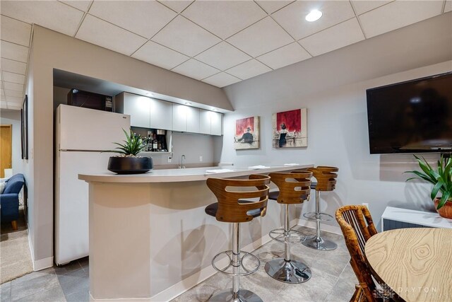 kitchen with kitchen peninsula, a kitchen bar, white cabinets, white refrigerator, and sink