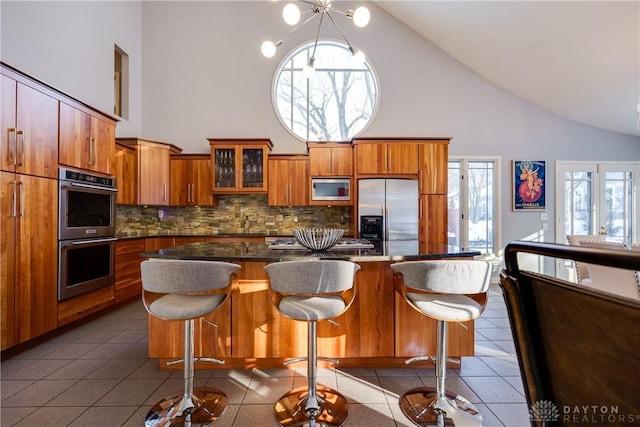 kitchen with a kitchen breakfast bar, stainless steel appliances, high vaulted ceiling, dark tile patterned flooring, and tasteful backsplash