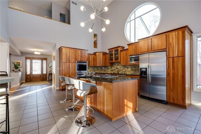 kitchen featuring stainless steel appliances, a kitchen island, a towering ceiling, and tasteful backsplash