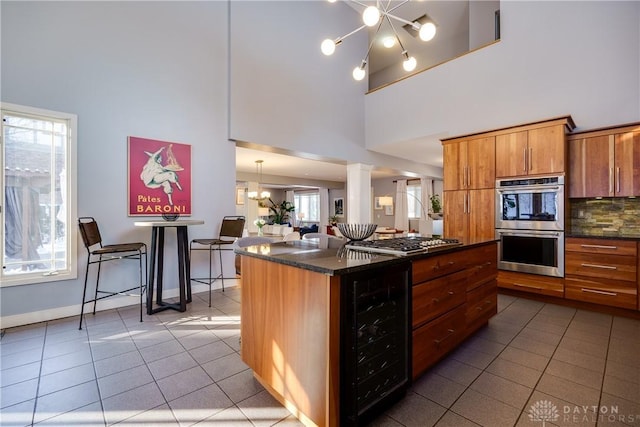 kitchen with an inviting chandelier, stainless steel appliances, decorative columns, a kitchen island, and beverage cooler