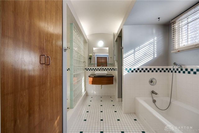 bathroom featuring sink, a bath, tile patterned flooring, and tile walls