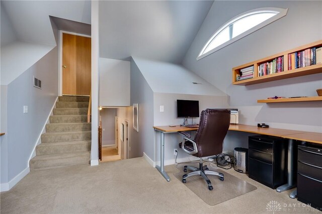 carpeted office featuring lofted ceiling and built in desk