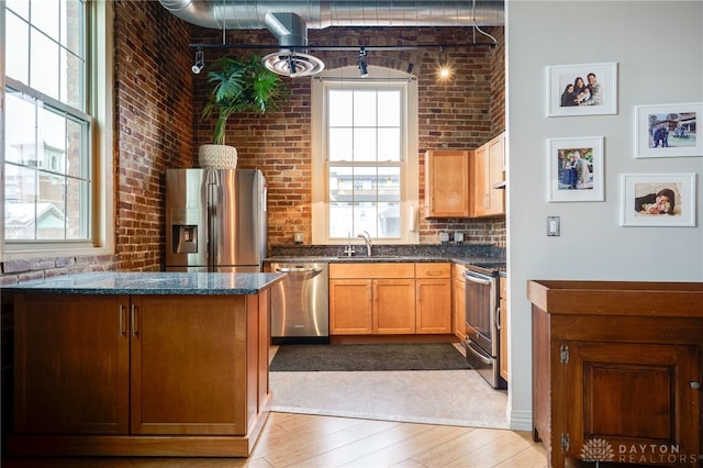 kitchen featuring light hardwood / wood-style floors, stainless steel appliances, brick wall, dark stone counters, and sink