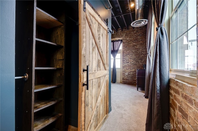 hallway with carpet floors, a barn door, and brick wall