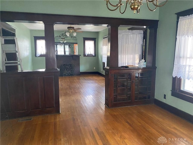 unfurnished dining area featuring ceiling fan with notable chandelier, decorative columns, and hardwood / wood-style flooring