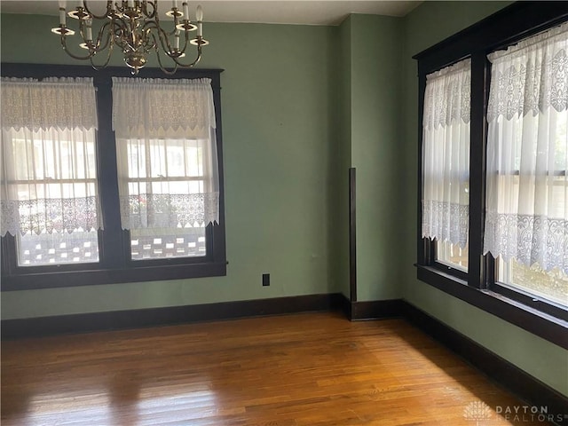 empty room featuring hardwood / wood-style floors, a healthy amount of sunlight, and a notable chandelier