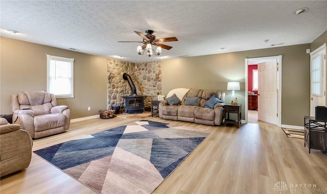 living room featuring a textured ceiling, ceiling fan, light hardwood / wood-style flooring, and a wood stove