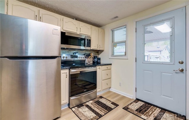 kitchen featuring a textured ceiling, light hardwood / wood-style flooring, stainless steel appliances, decorative backsplash, and white cabinetry