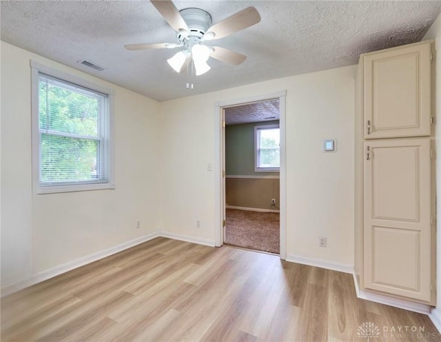 empty room with light hardwood / wood-style floors, a textured ceiling, ceiling fan, and a healthy amount of sunlight