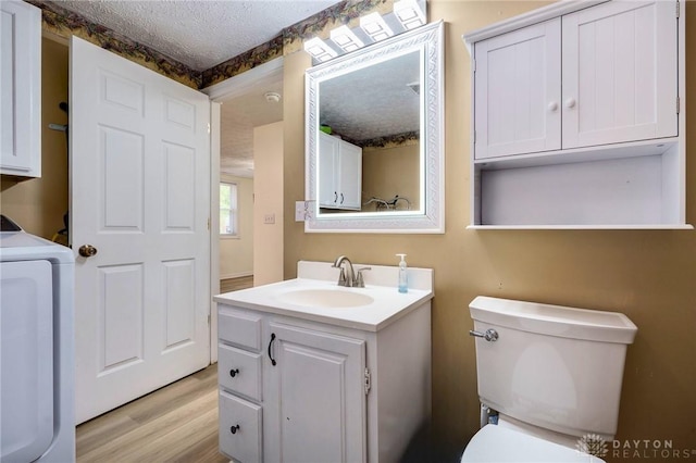 bathroom featuring toilet, a textured ceiling, washer / clothes dryer, wood-type flooring, and vanity